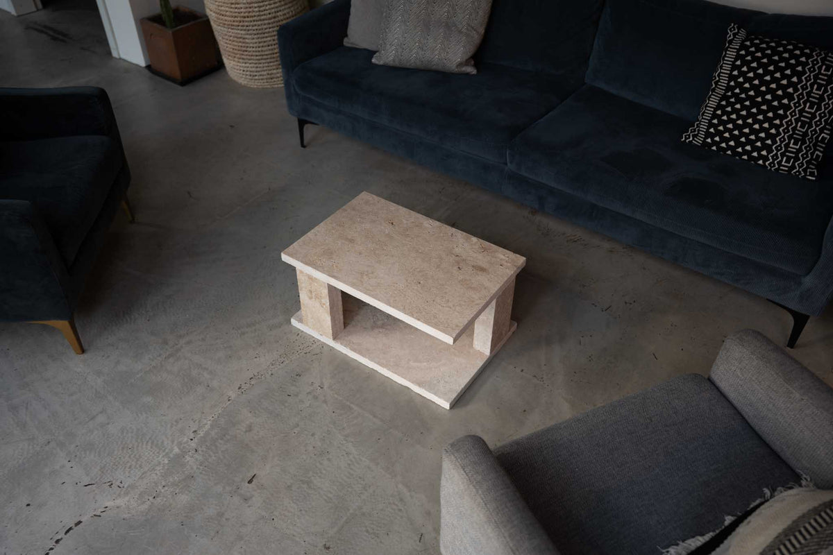 Bold Couchtisch aus Travertin vor einem dunkelblauen Sofa im Wohnzimmer